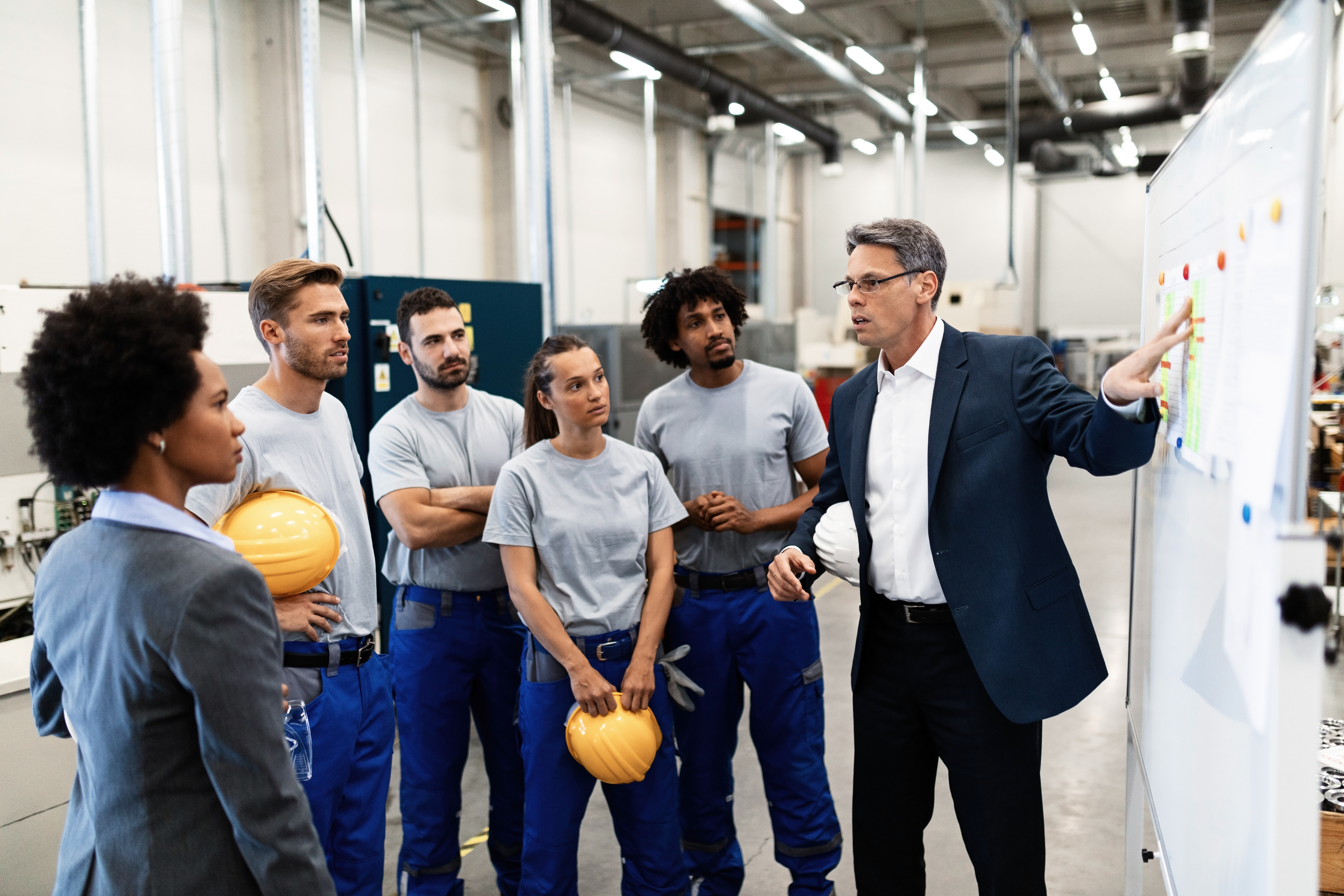 Mature businessman explaining new strategy plans to group of employees in a factory.